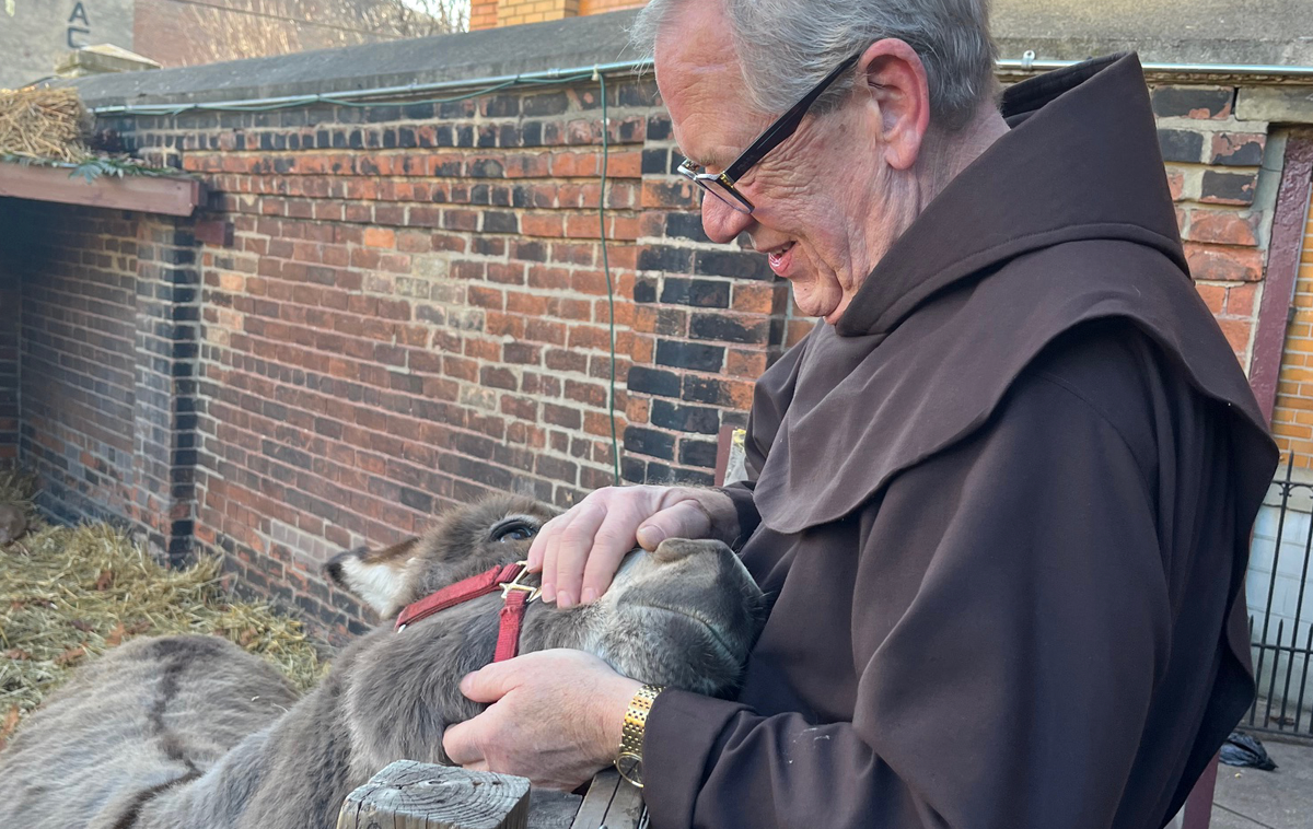 A friar cradles a happy-looking donkey's head in his hands