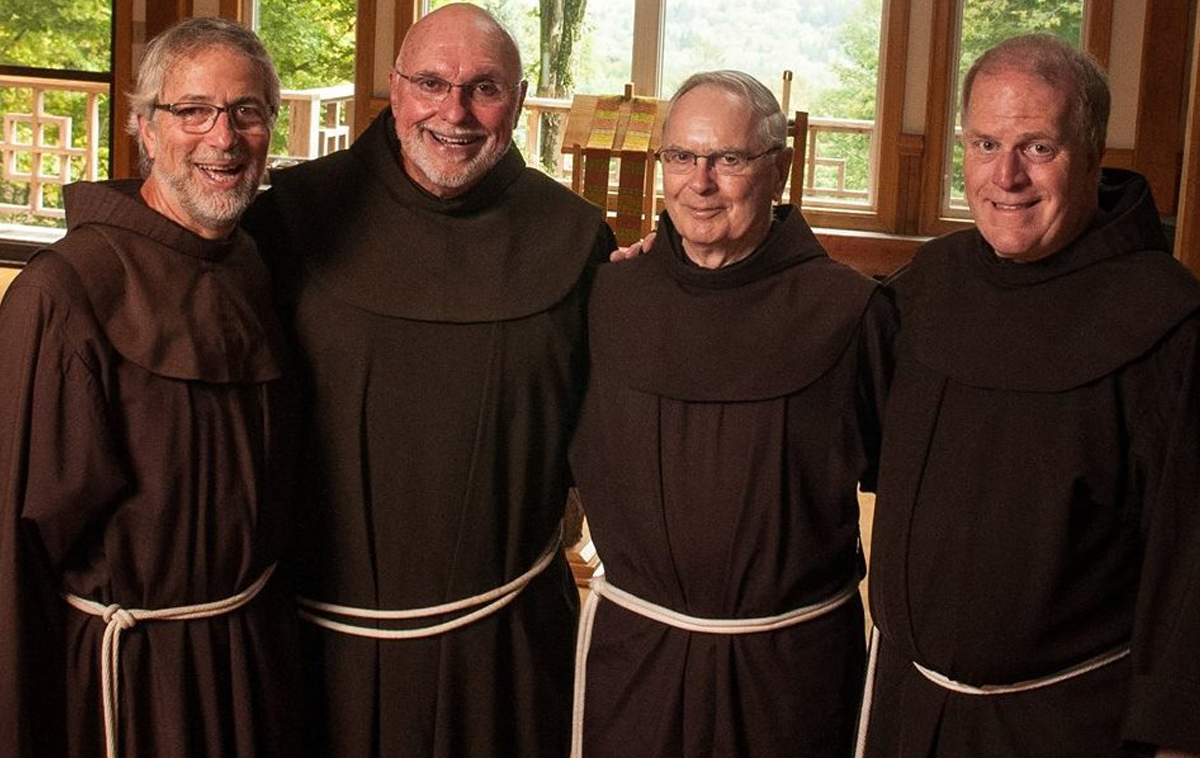 Group photo of four Franciscan friars in a wooden chapel