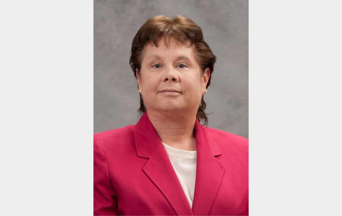 A headshot of a woman wearing a pink blazer with a white shirt beneath