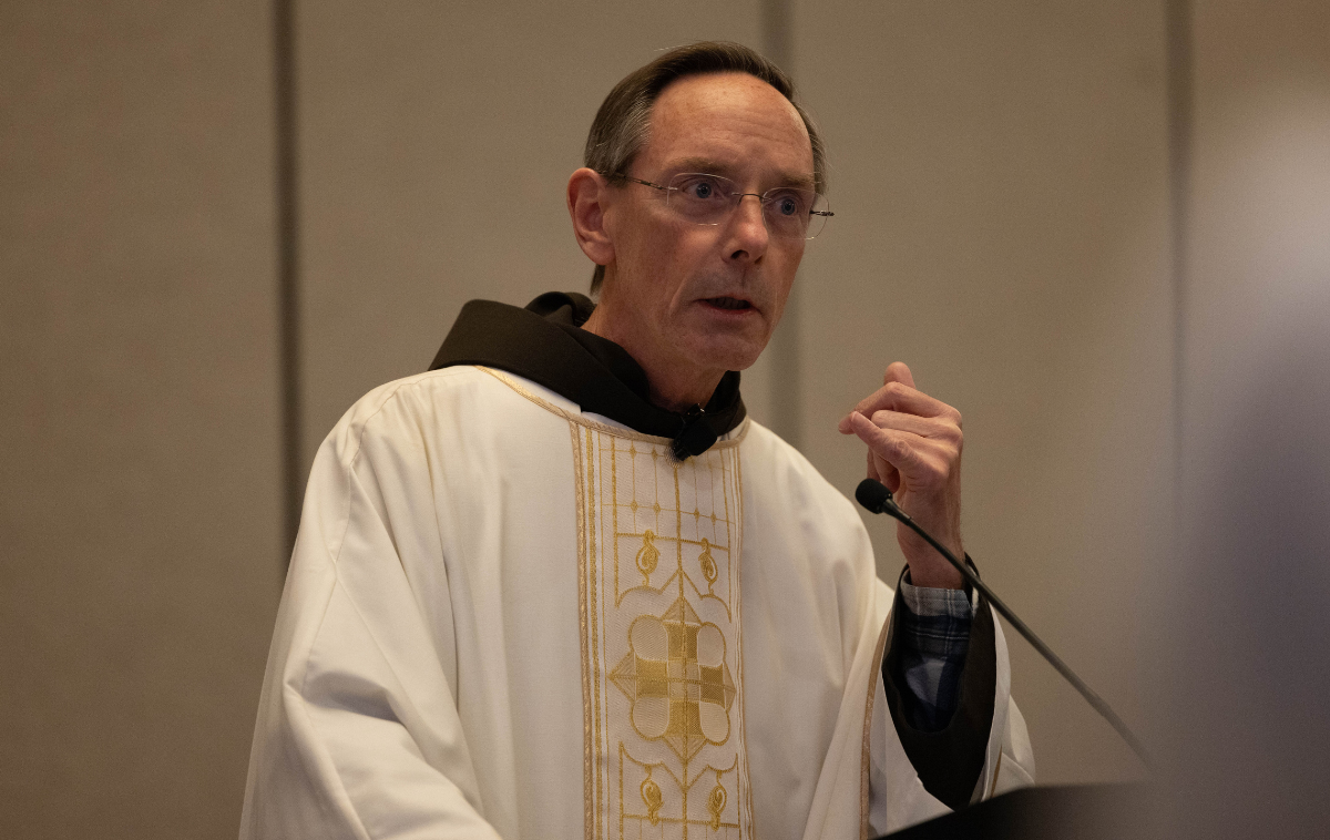 A man wearing eyeglasses and vestments speaks at a podium.