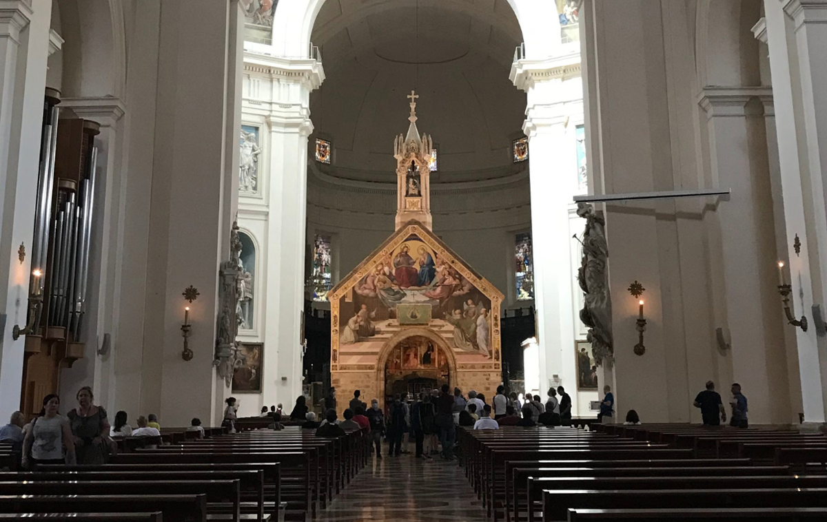 A little medieval church made of stone stands at the center of an enormous Renaissance-style basilica.