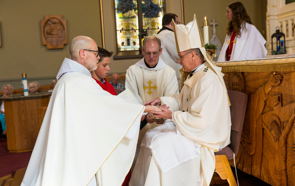 A priest anoints a man who is kneeling before him.