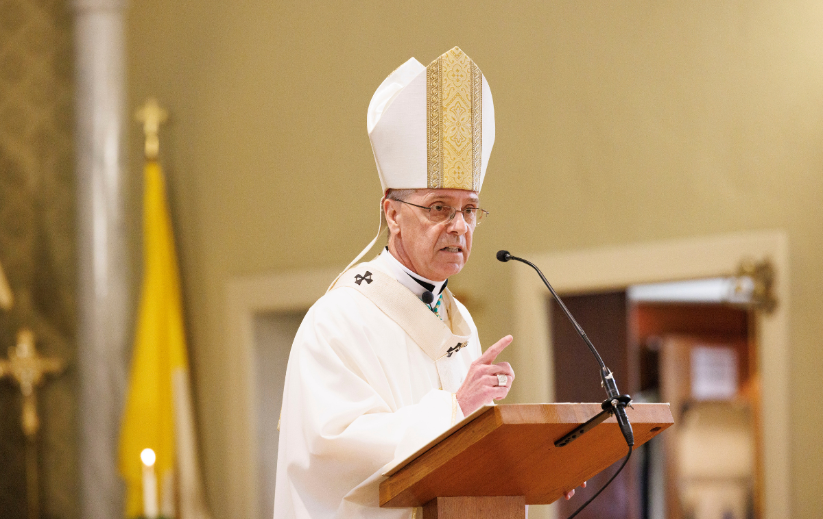 A man wearing vestments delivers a homily at a podium.