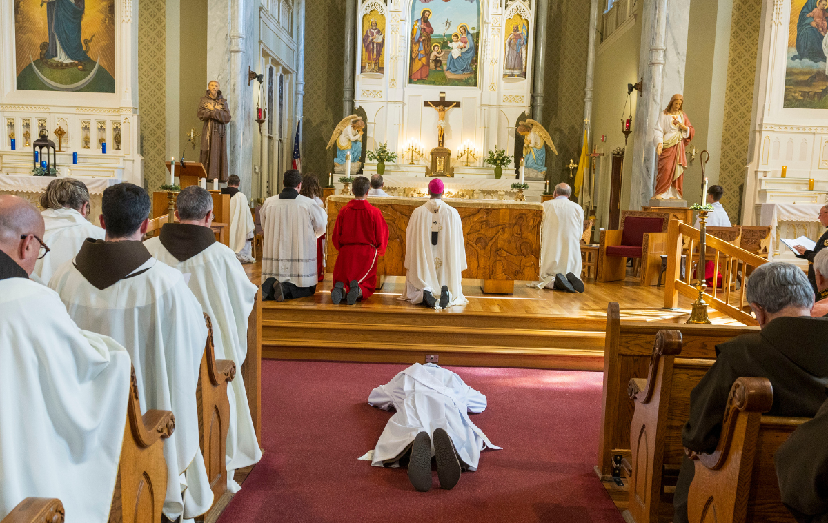 A man lays on his stomach in front of an altar in a Catholic church.