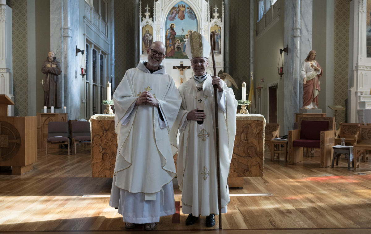 a priest stands for a photo with an archbishop in a Catholic church.