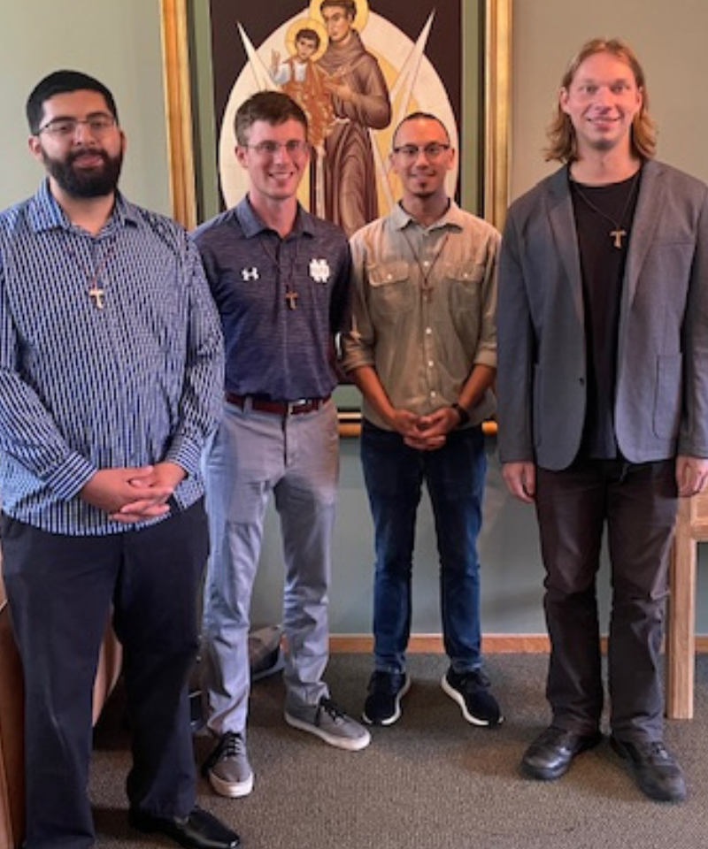 Four men pose for a photograph in front of an image of a saint.