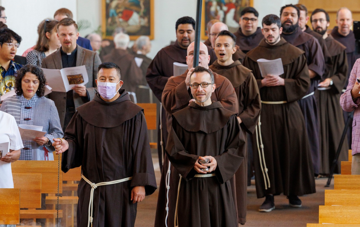 A line of Franciscan friars wearing brown habits process into a church.