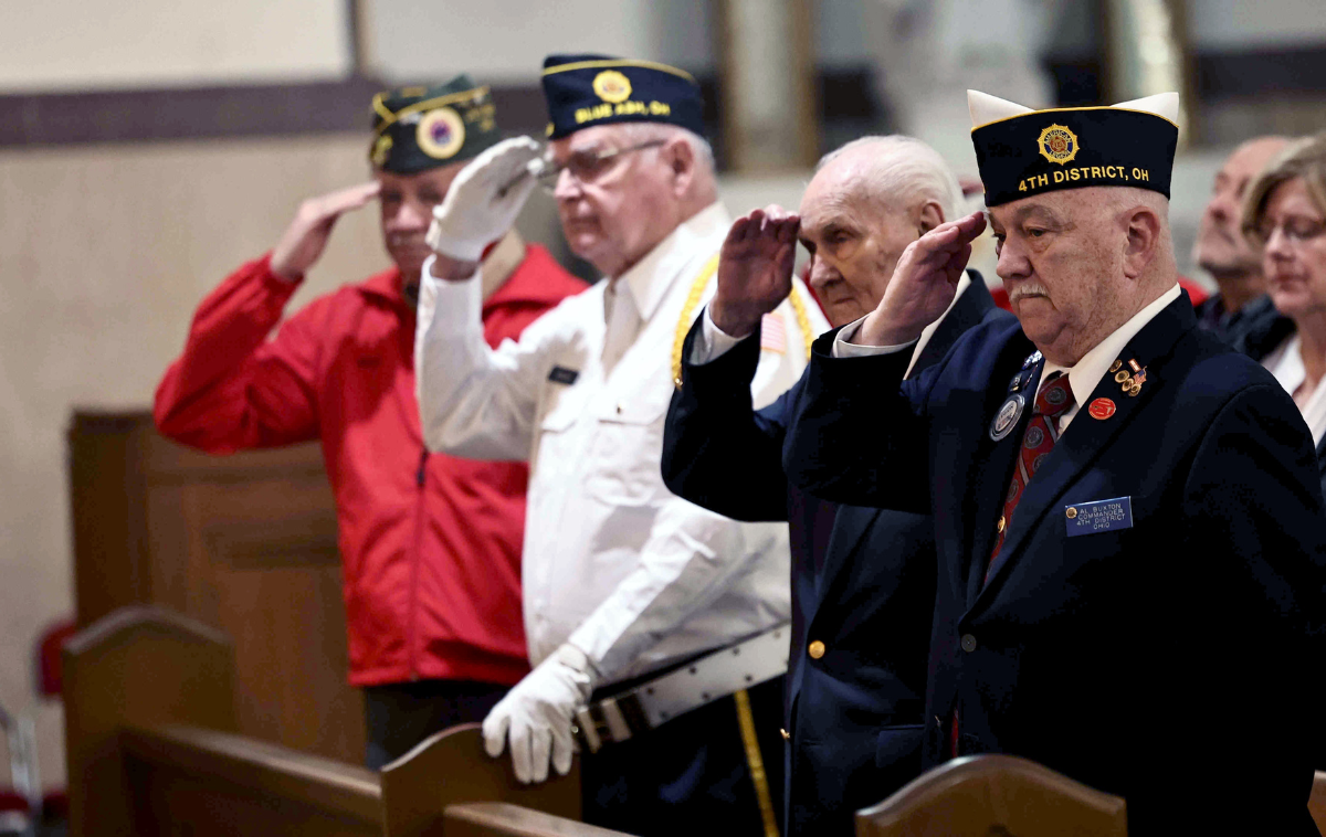Veterans in uniform salute as they stand in the pews of a church