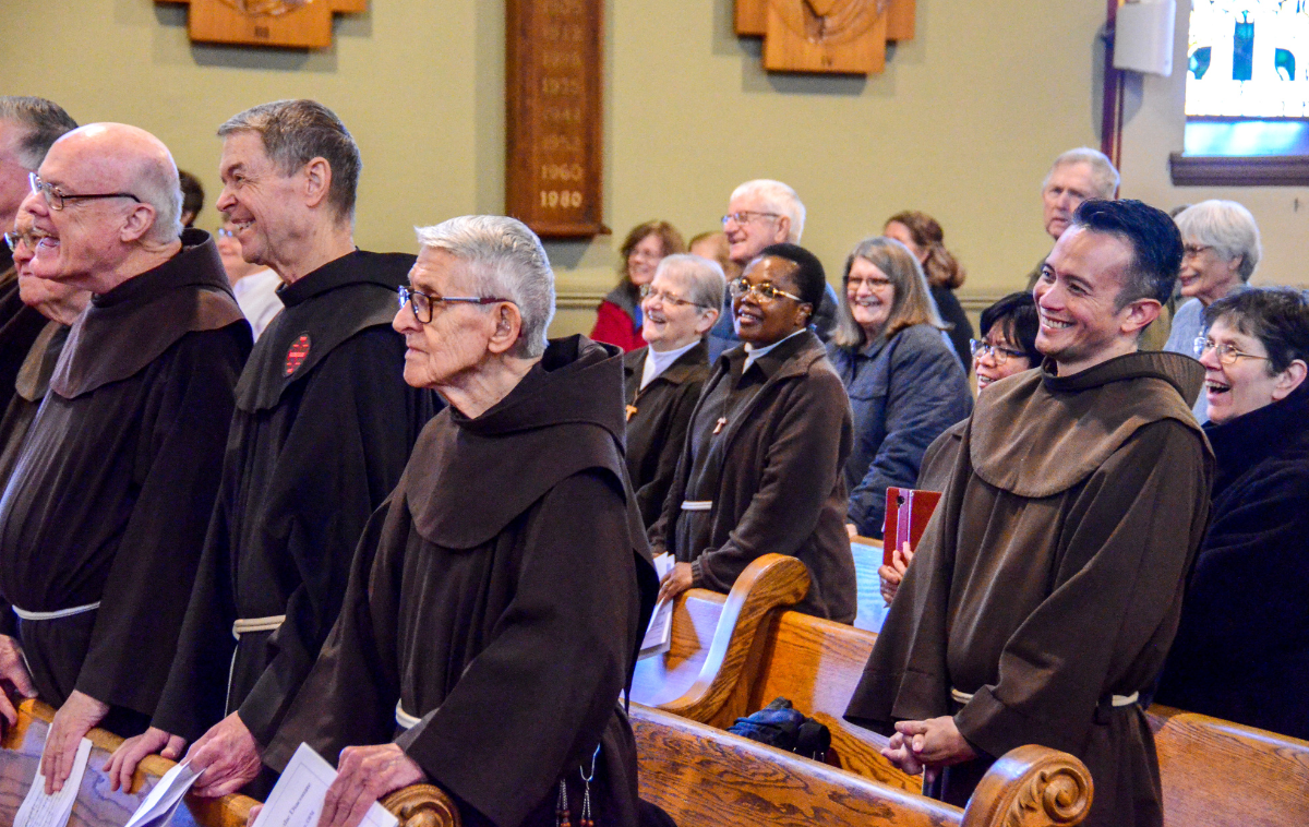 A group of smiling friars and parishioners standing in the pews of a church