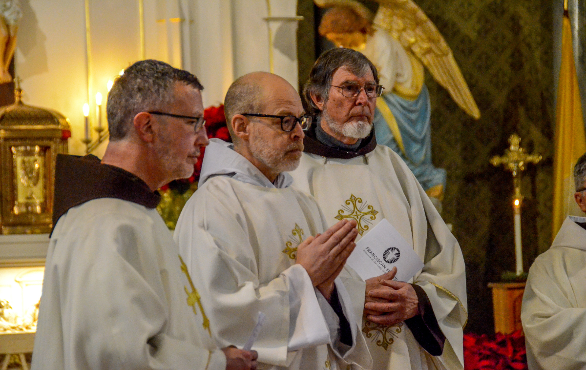 A deacon lifts his hands in his prayer as he stands between two priests