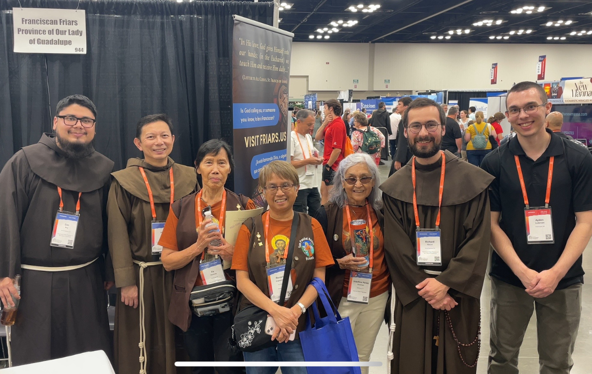 A group of friars and people attending the Eucharistic Congress smile at the camera.