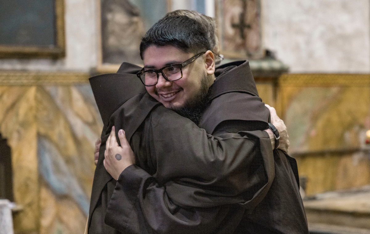 Two friars smile as they share a hug.