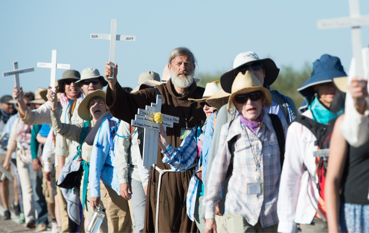 A line of people carrying white wooden crosses walks through the Arizona desert.