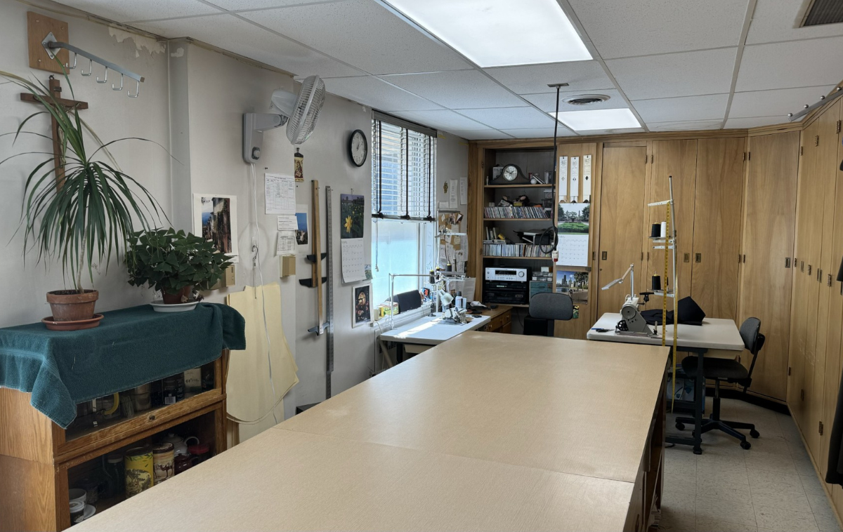 A tailor's shop. In the center of the room is a long table, twice the length of a grown man. Sewing machines sit on small tables that line the walls.