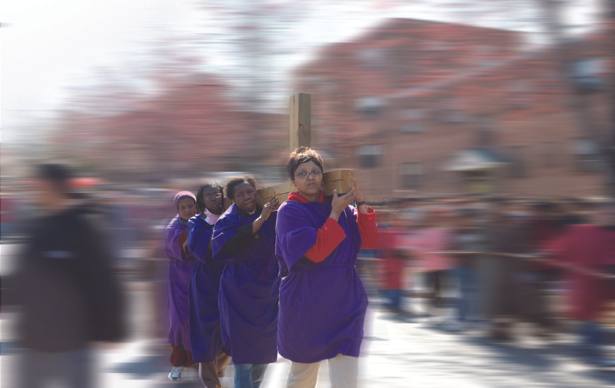 four people wearing purple robes carry a cross through the streets