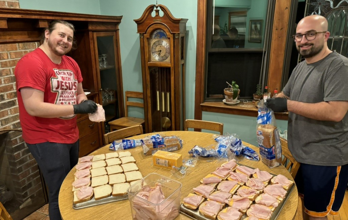 Two young men smile as they make ham and cheese sandwiches