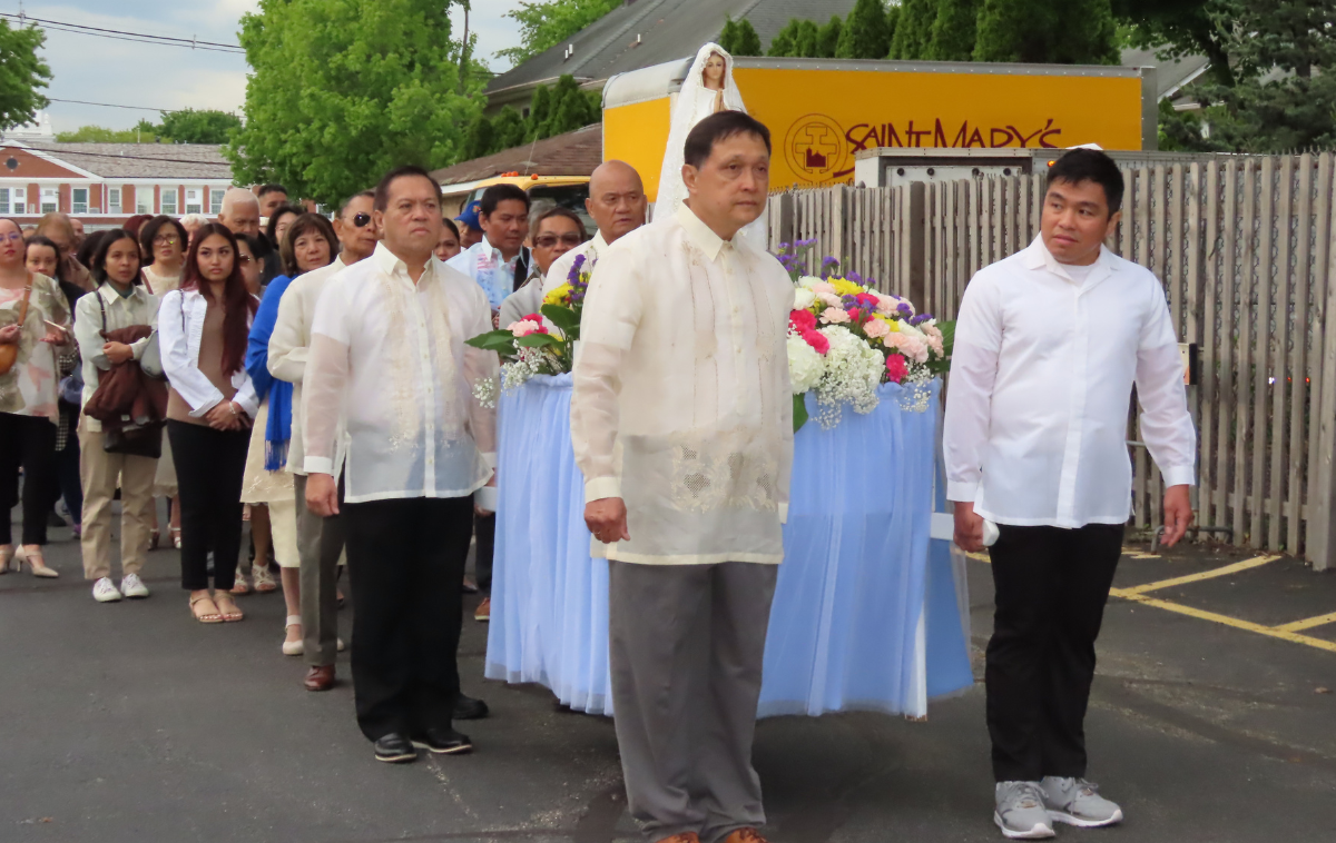 Parishioners carry a statute of Mary surrounded by flowers on a platform down a residential street