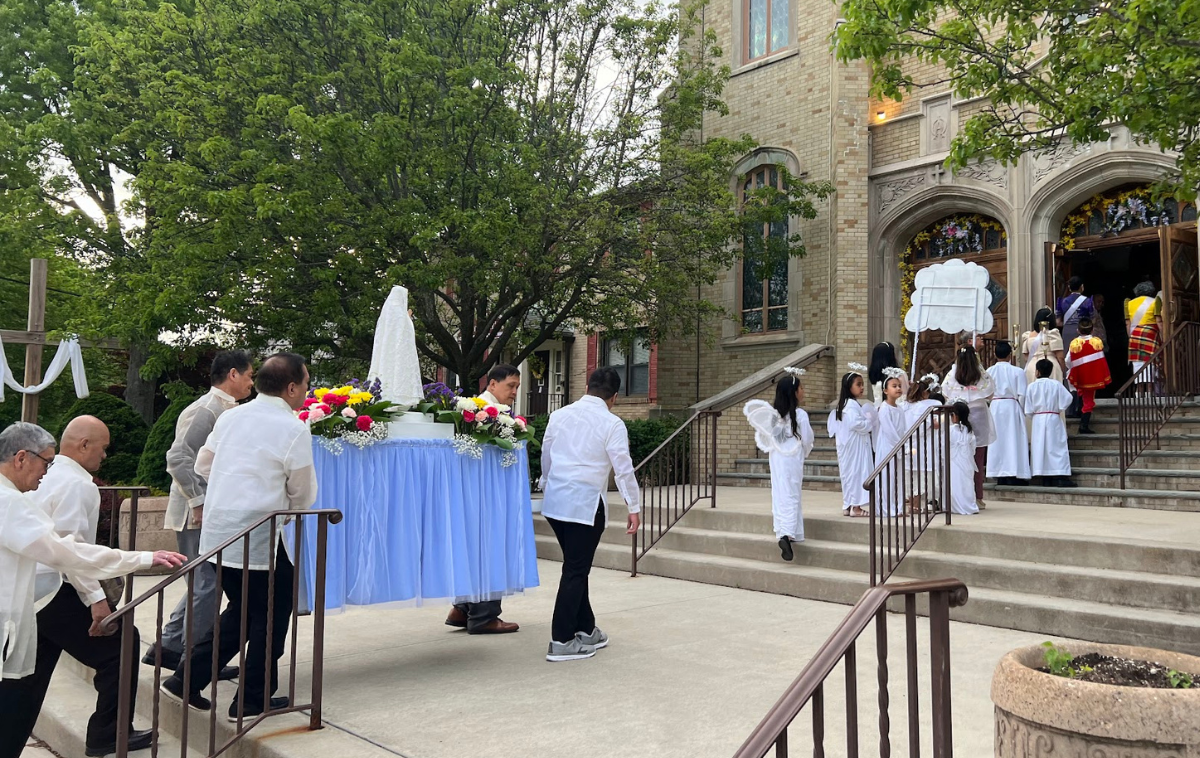 People carry a statue of Mary surrounded by flowers into a church.