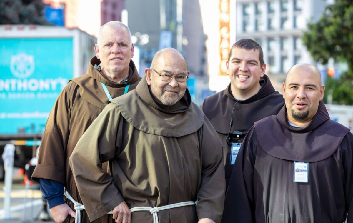 Four friars wearing their habits stand in a street in San Francisco and smile at the camera