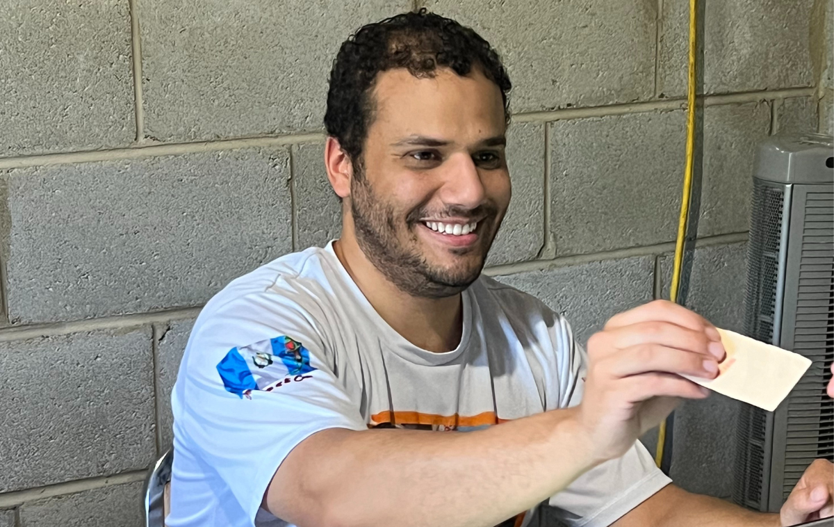 A smiling young adult man with a beard hands a white ticket to a guest.