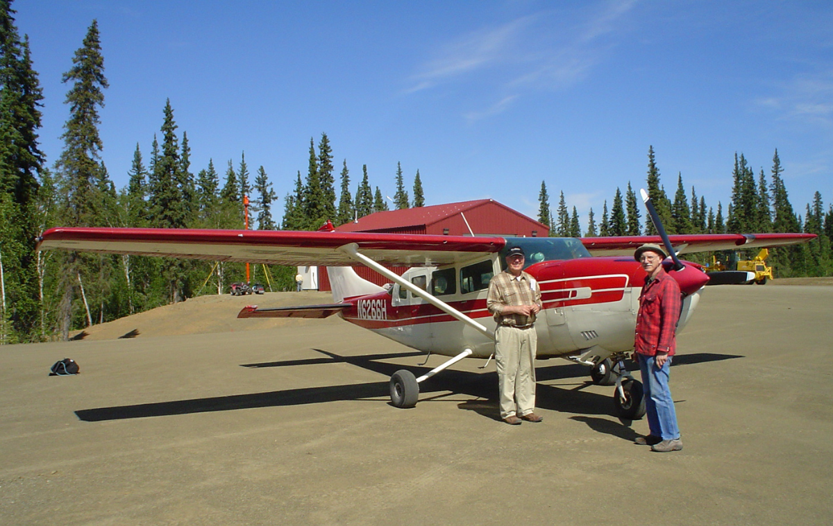 Two men stand beside a red and white propeller plane.