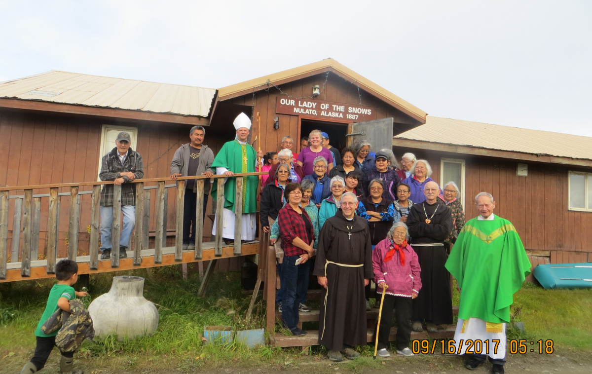 A group of people of all ages stand on the wooden steps of a church.