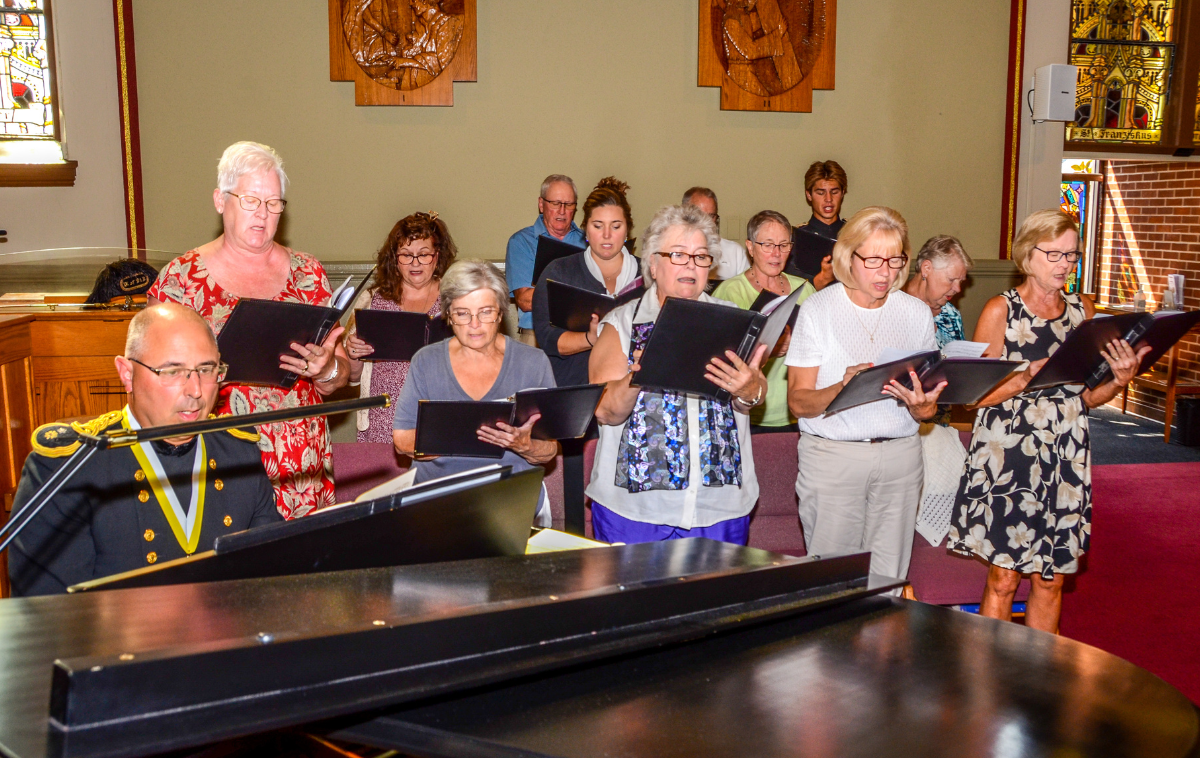 A choir sings as a man accompanies them on piano.