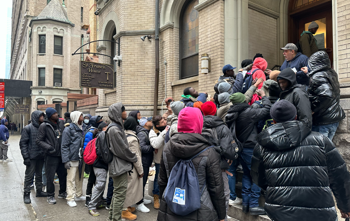 Several people in winter clothing stand in line on a stairway and along a sidewalk.