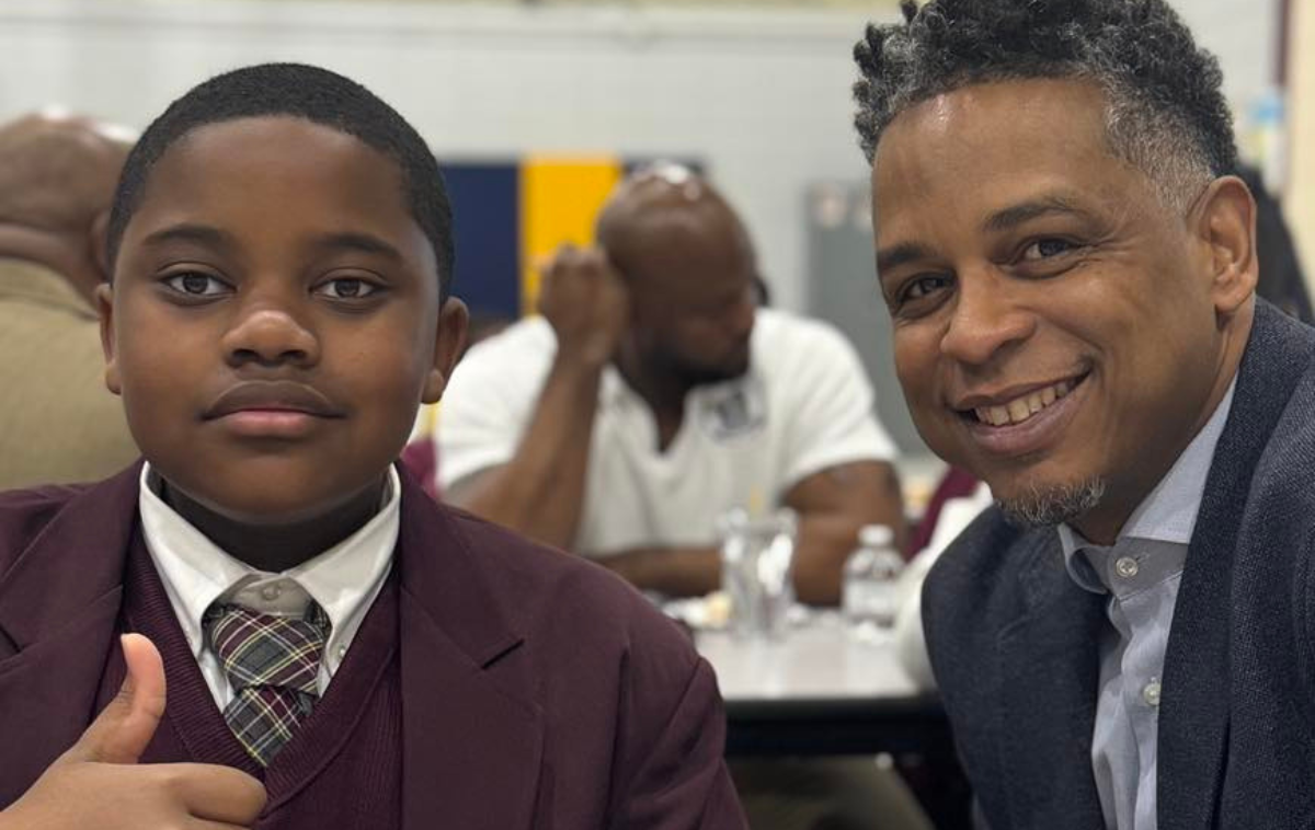 A child gives a thumbs up as he sits next to an older man.