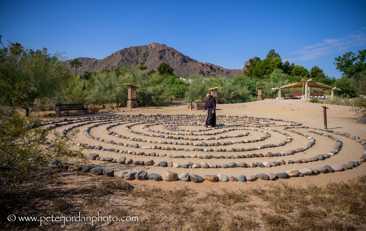 A friar walks along a stone labyrinth in the desert.