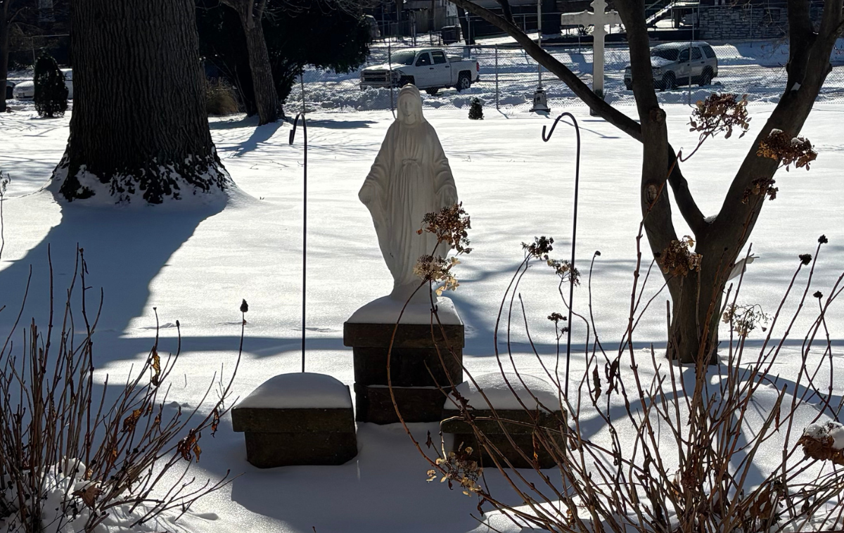 A white statue stands on the tallest of three platforms amid a snowy landscape.