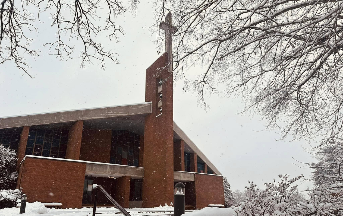 A church with a steeple and snow on the ground and trees in front of it.