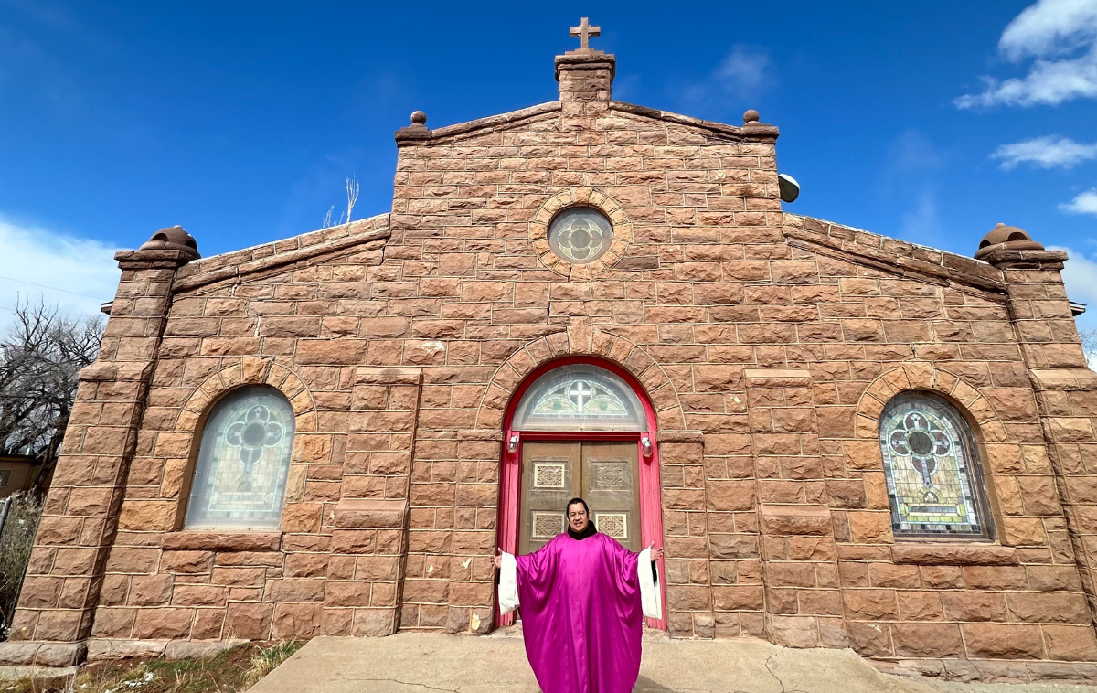 A friar wearing purple vestments stands in front of Our Lady of Fatima Church.