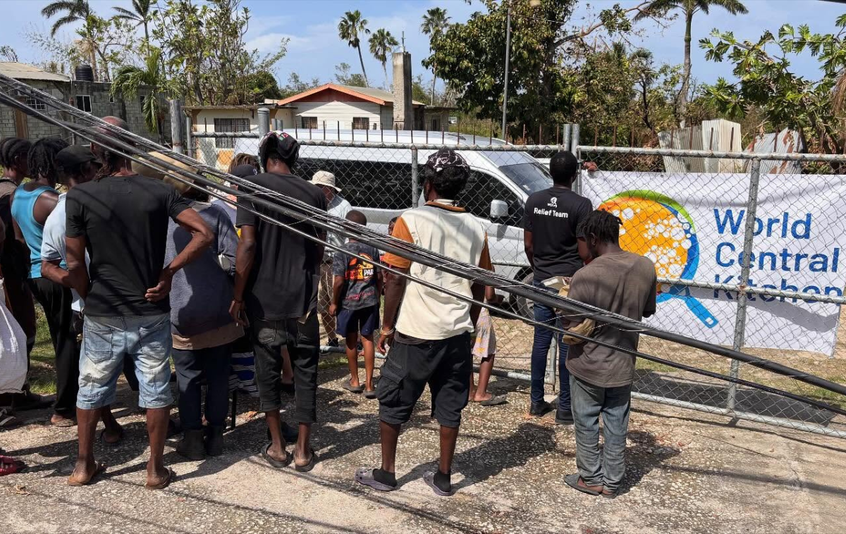 A friar welcomes three people who are picking up bags of food.