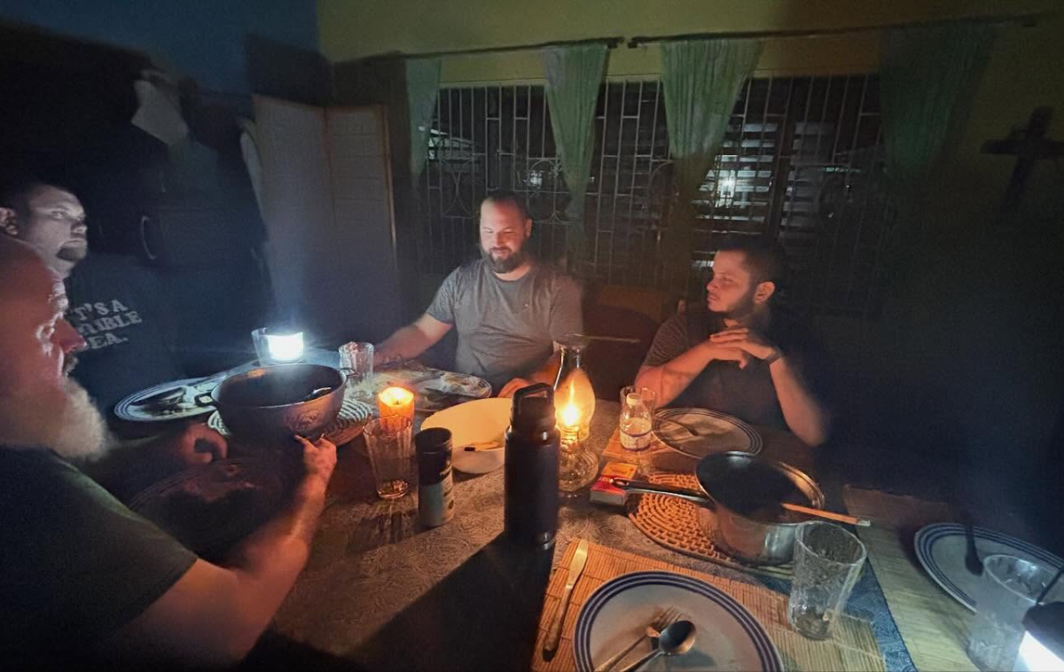 A friar welcomes three people who are picking up bags of food.