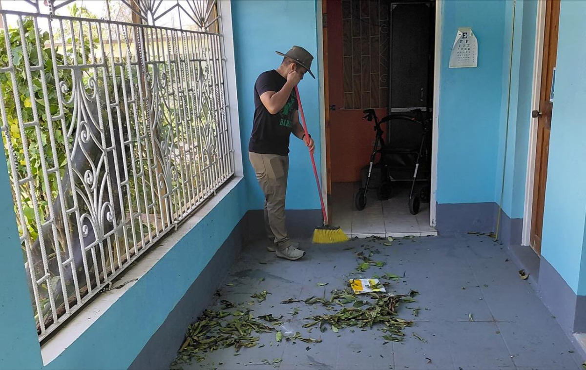 A friar welcomes three people who are picking up bags of food.