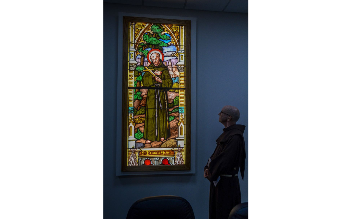 Also present are stained glass windows of St. Francis and St. Patrick, both originally installed in the Third Order chapel at St. Patrick Church in Buffalo, New York, in 1892. The friars ministered there from 1858 to 1981, when the parish merged with St. Rita's. The windows were moved to St. Patrick's Friary, where the friars continued to serve until 2024. In this photo, Br. Jud Weiksnar, OFM, who served in Buffalo before moving to Cincinnati, is pictured here with the window of St. Francis. (Photo courtesy of Br. Frank Jasper, OFM)