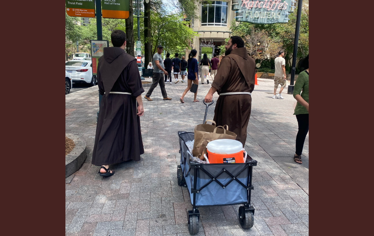Several days a week, the friars walk the streets of Uptown Charlotte with a wagon of ice-cold water and peanut butter and jelly sandwiches prepared by parishioners of St. Peter Catholic Church. Earlier that afternoon, one man waved over Brothers Casey and Tito for water and candy. "I love it when yar'all come out," he said. "I get my favorite snack: peanut butter and jelly." (Photo by Eli Pacheco)