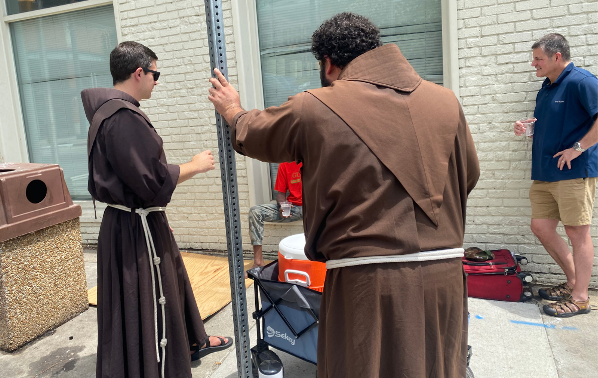 Most encounters on sandwich days are brief. Others, revealing. Brothers Casey and Tito heard about one man's happy news about his family. The man on the right was a passerby who'd stopped to talk to the man before. (Photo by Eli Pacheco)