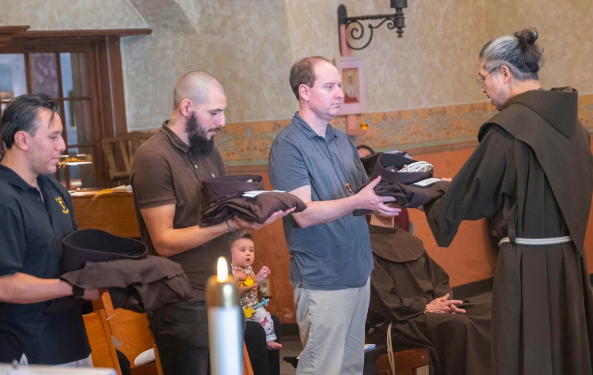 Br. Michael Reyes, OFM, presents Br. Jason Stoodley, OFM, a habit. The Franciscan habit is modeled after the simple tunic worn by St. Francis of Assisi, the founder of the Order of the Friars Minor. (Photo by Br. Paul Chelus, OFM)