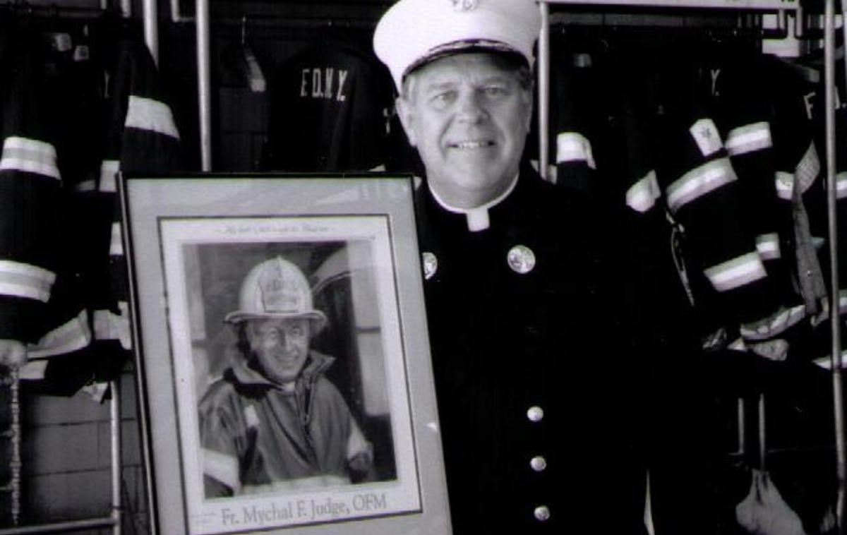 A smiling man in formal fire department uniform stands next to a photo.