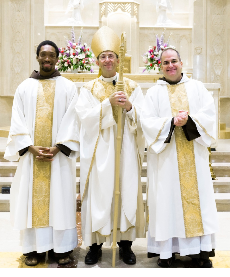 A bishop stands between two deacons in the front of a church.