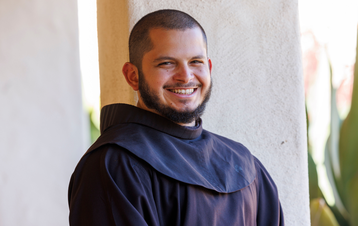 A smiling, bearded man wearing a friar habit poses for a photo.