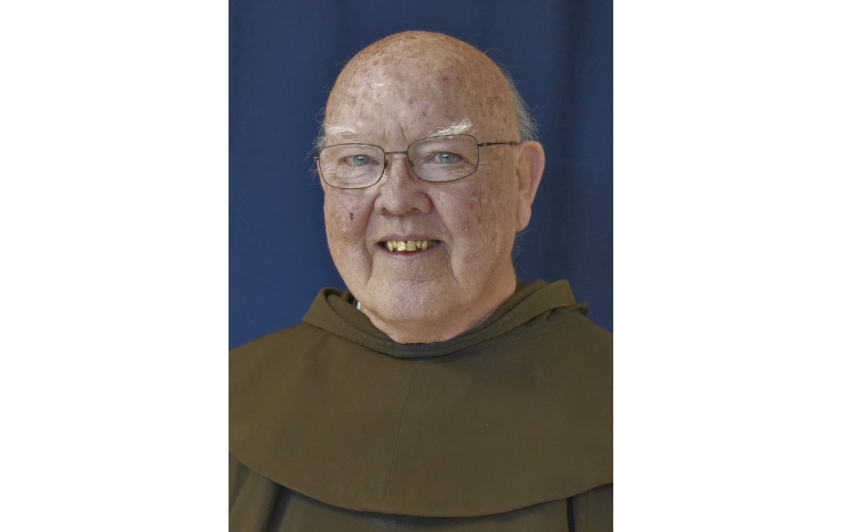 A smiling man wearing eyeglasses and a friar habit poses for a photo.