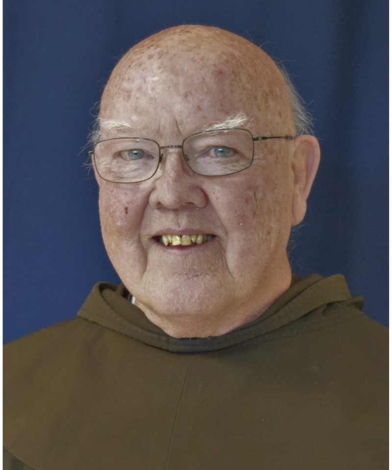 A smiling man wearing eyeglasses and a friar habit poses for a photo.