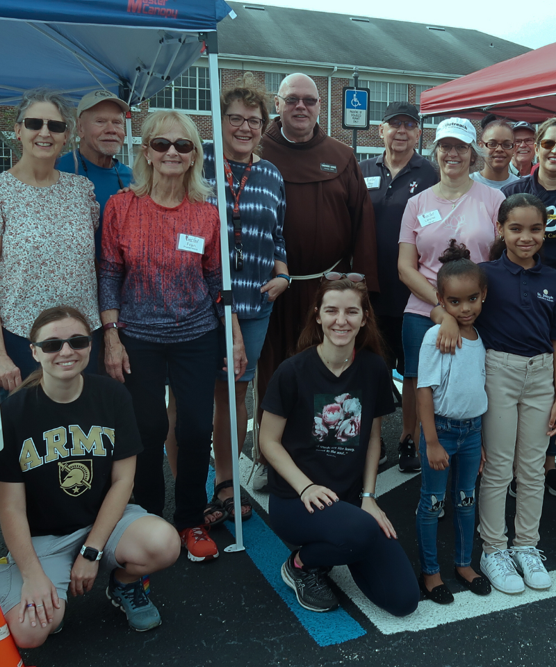 A group of volunteers, men, women, and children, pose for a photo outside, some under a tent.