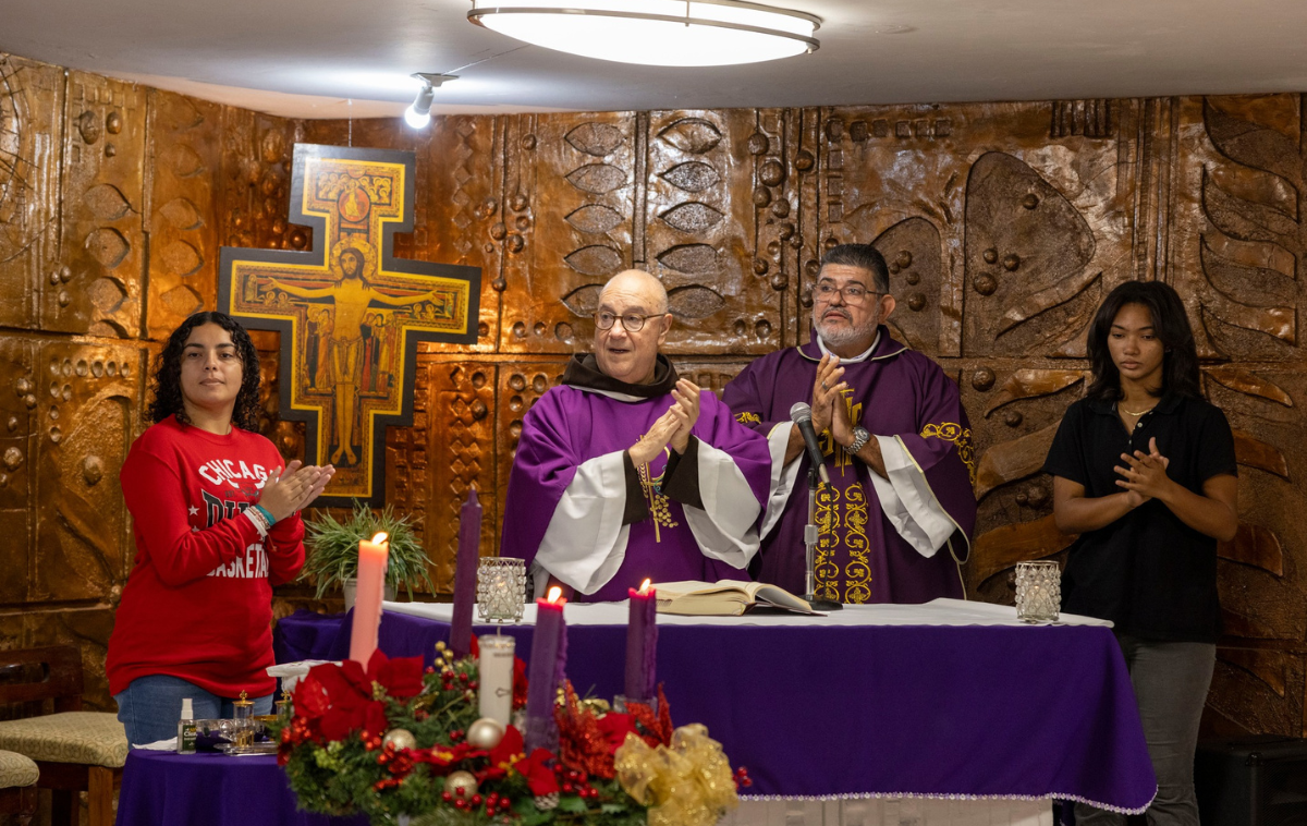 A priest performs mass in white and gold vestments with four clergy behind him.